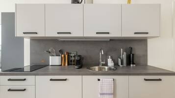 A modern kitchen with white cabinets, a stainless steel sink, and a coffee maker.