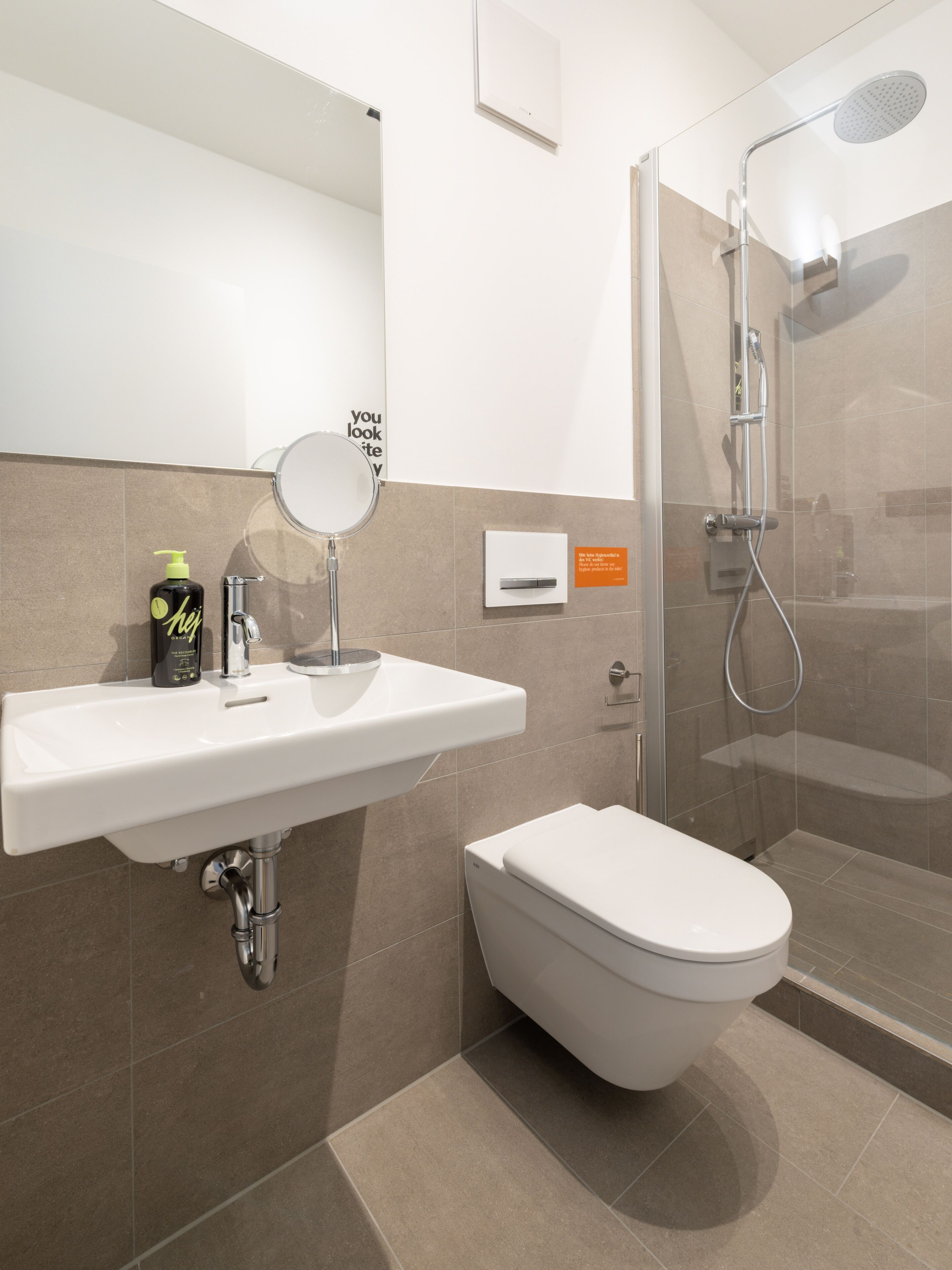 Un bany modern amb un lavabo, un mirall i un vàter de color blanc.