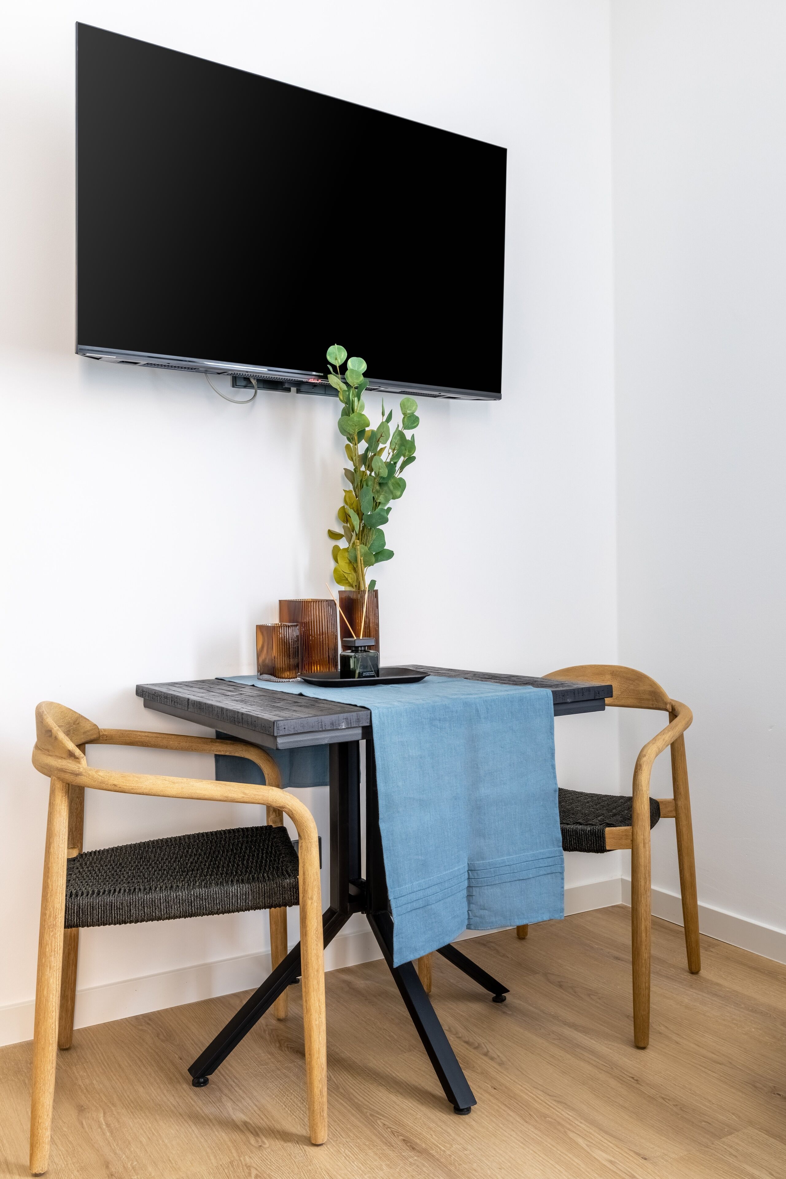 Un espace repas moderne comprenant une table, deux chaises, un téléviseur fixé au mur et une plante en pot.
