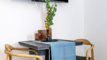 Un espace repas moderne comprenant une table, deux chaises, un téléviseur fixé au mur et une plante en pot.