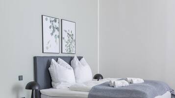 A modern bedroom with a grey bed, white pillows, a grey throw blanket, and two framed botanical prints on the wall.