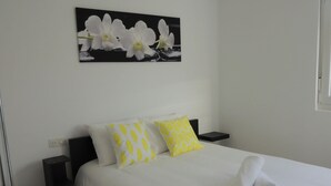Habitación de hotel con cama, almohadas, un cuadro de orquídeas e íconos que indican servicios como estacionamiento gratuito, ubicación, Wi-Fi, control de desinfección O3 y una cuenta gratuita de Netflix.