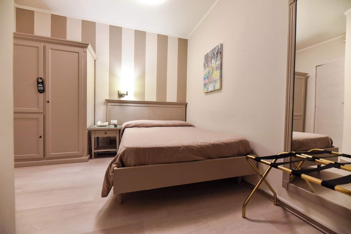 A bedroom with a bed, a nightstand, a dresser, a mirror, and a striped wall.
