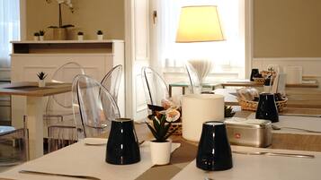 A dining area with clear chairs, a table set with cutlery, a lamp, and a basket of bread.