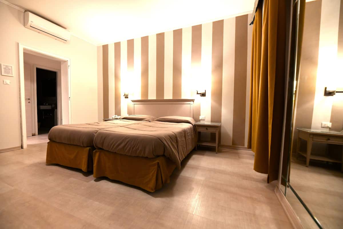 A hotel room with a large bed, bedside tables, a mirror, and a door leading to another room.