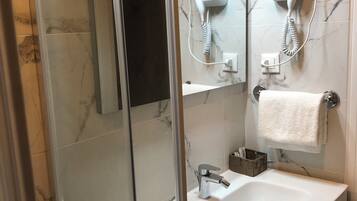 Een moderne badkamer met een douchecabine van glas, een witte wastafel en twee haardrogerhouders aan de muur.