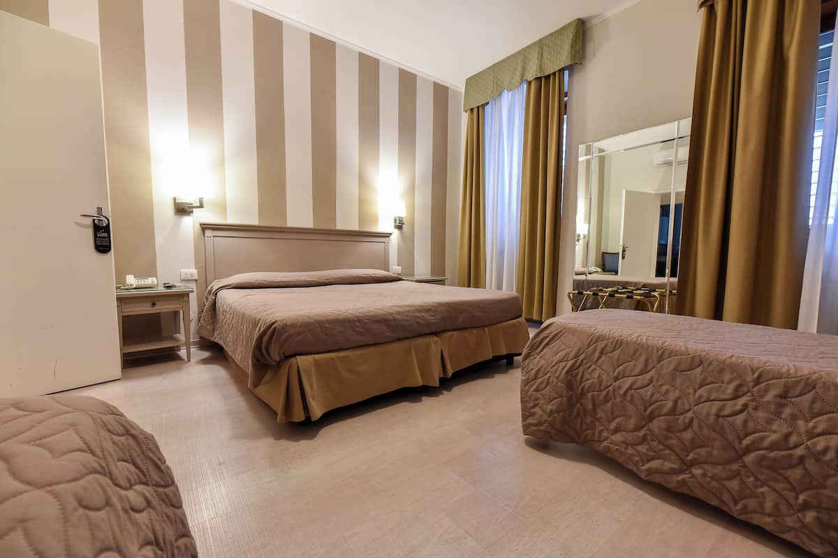 A hotel room with two beds, a nightstand, a mirror, and striped walls.