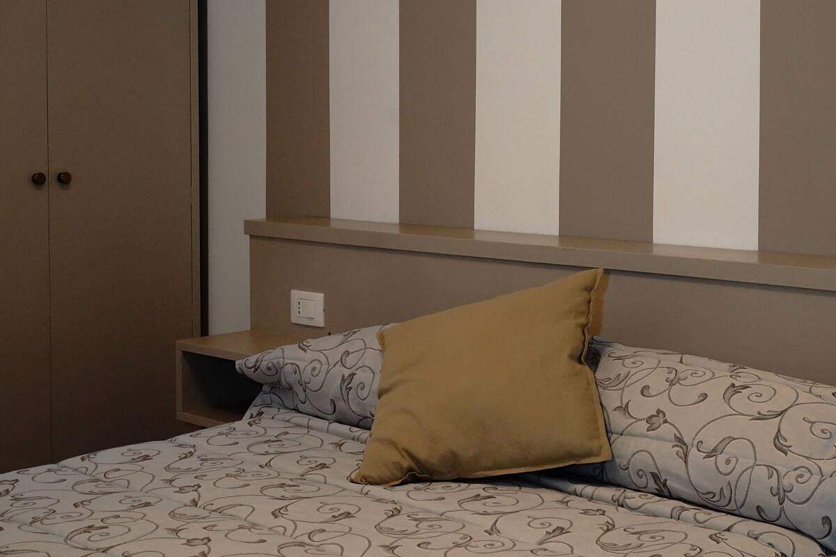 A bedroom with a bed, a nightstand, a wardrobe, and a window with vertical blinds.
