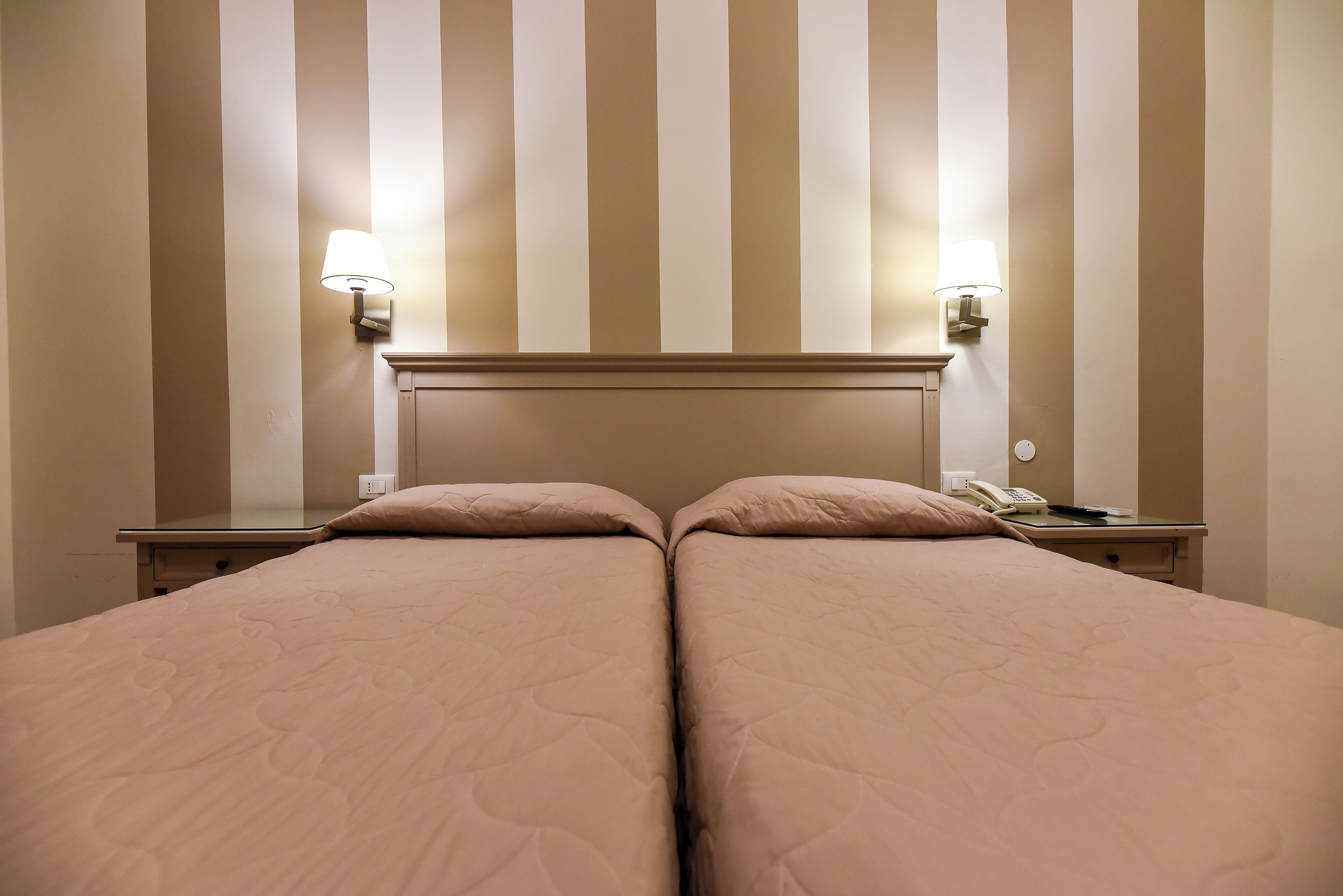 Una cama doble con cabecera, dos mesitas de noche con lámparas y un teléfono en una de ellas.
