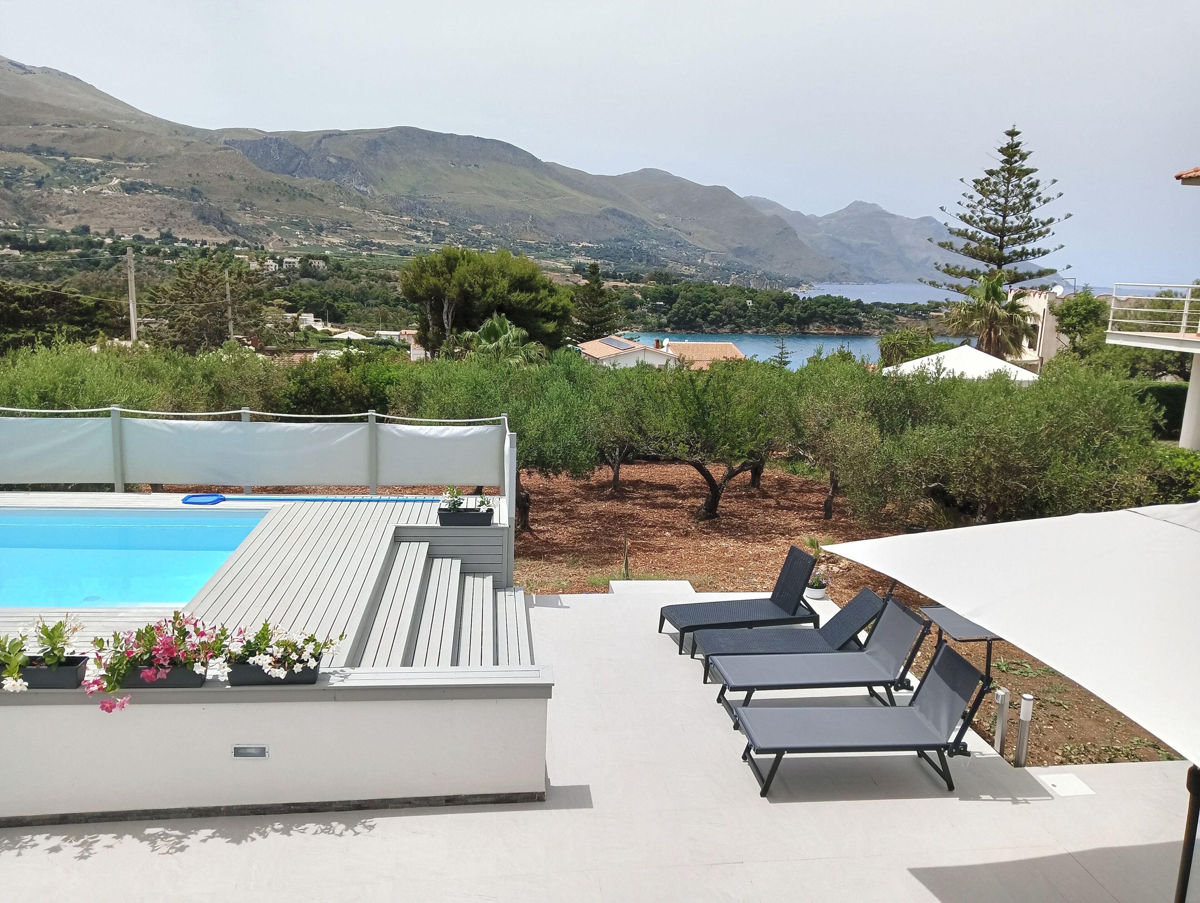 Zona de piscina con sillones de descanso y vistas al mar y a las montañas.
