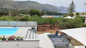 Zona de piscina con sillones de descanso y vistas al mar y a las montañas.