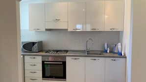 Una cocina compacta con armarios blancos, microondas, cocina a gas y horno empotrado.