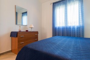 A bedroom with a bed, a dresser, a mirror, and a window with curtains. - Villa Corallo - Scopello Guidaloca Bay  (Castellammare del Golfo)