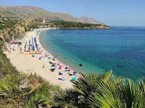 A beach with clear blue water, a row of umbrellas, and a mountainous backdrop. - Villa Corallo - Scopello Guidaloca Bay (Castellammare del Golfo)