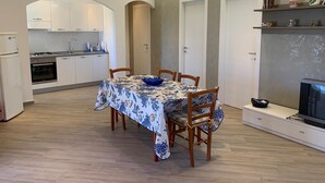 Una cocina moderna con armarios blancos, una mesa de comedor con mantel floreado azul y un televisor integrado.
