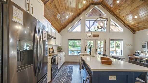 A spacious kitchen with a large island, wooden ceiling, and large windows offering views of the outdoors. - A Rustic Cabin with a Modern Twist w Hot Tub,Fire Pit,Fireplace,Near Lake Sleep7 (Broken Bow)