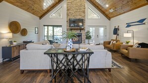 A spacious living room with a high ceiling, a stone fireplace, and modern furniture. - A Rustic Cabin with a Modern Twist w Hot Tub,Fire Pit,Fireplace,Near Lake Sleep7 (Broken Bow)