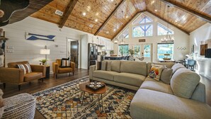 A spacious living room with a high wooden ceiling, a large window, and a cozy seating area. - A Rustic Cabin with a Modern Twist w Hot Tub,Fire Pit,Fireplace,Near Lake Sleep7 (Broken Bow)