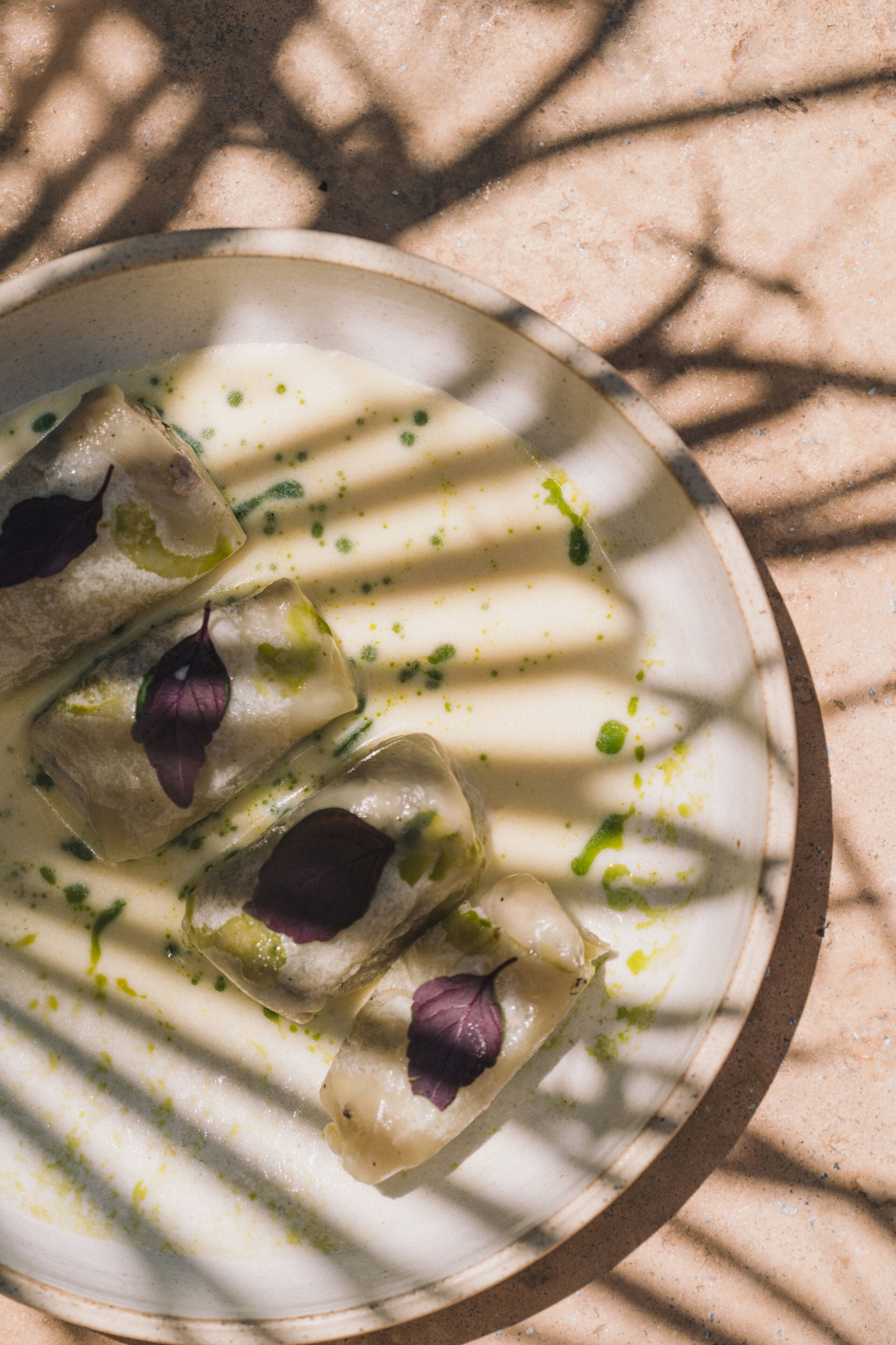A plate of ravioli with a creamy sauce and green herbs, served on a ceramic plate.