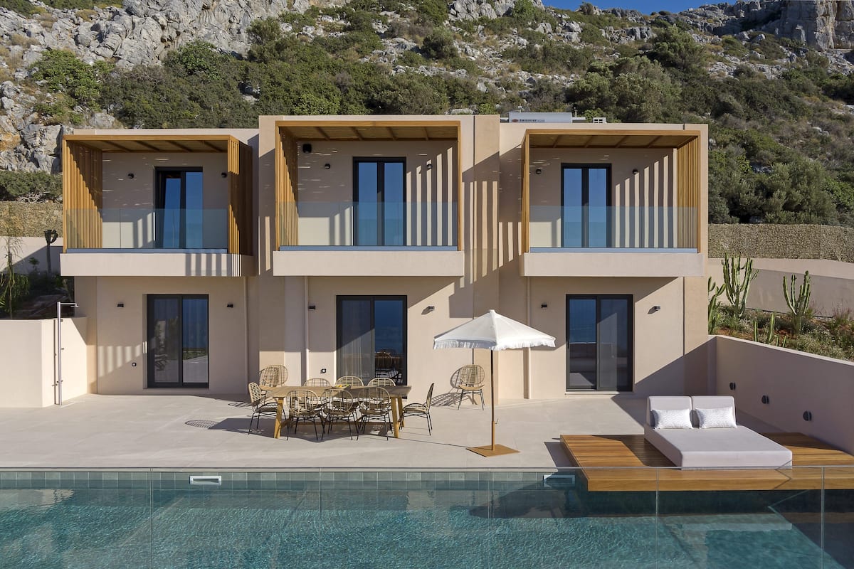 A modern two-story house with a swimming pool, outdoor furniture, and a view of rocky hills.