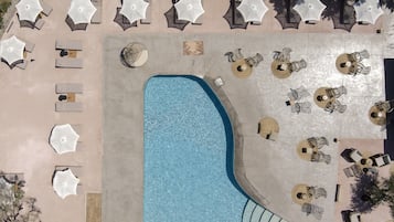 An aerial view of a pool area with lounge chairs and umbrellas arranged around the pool.