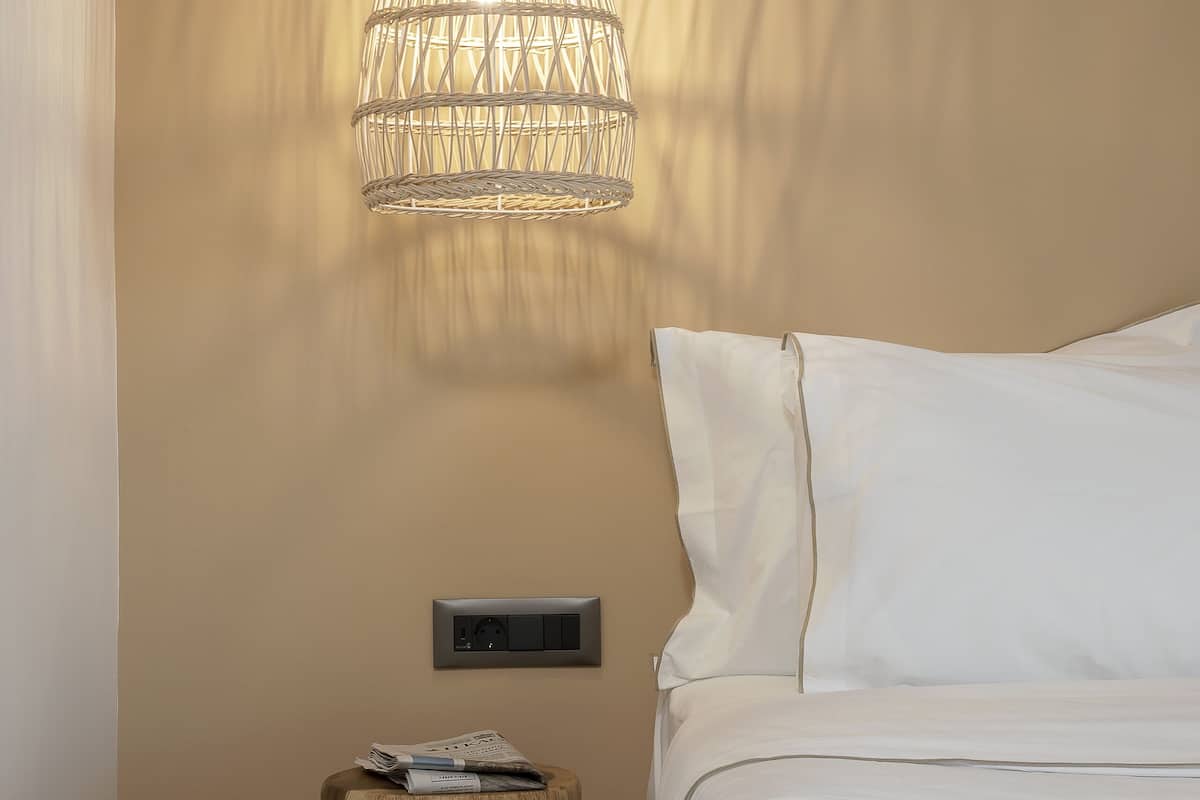 A neatly made bed with white linens, a bedside table with a magazine, and a hanging light fixture.