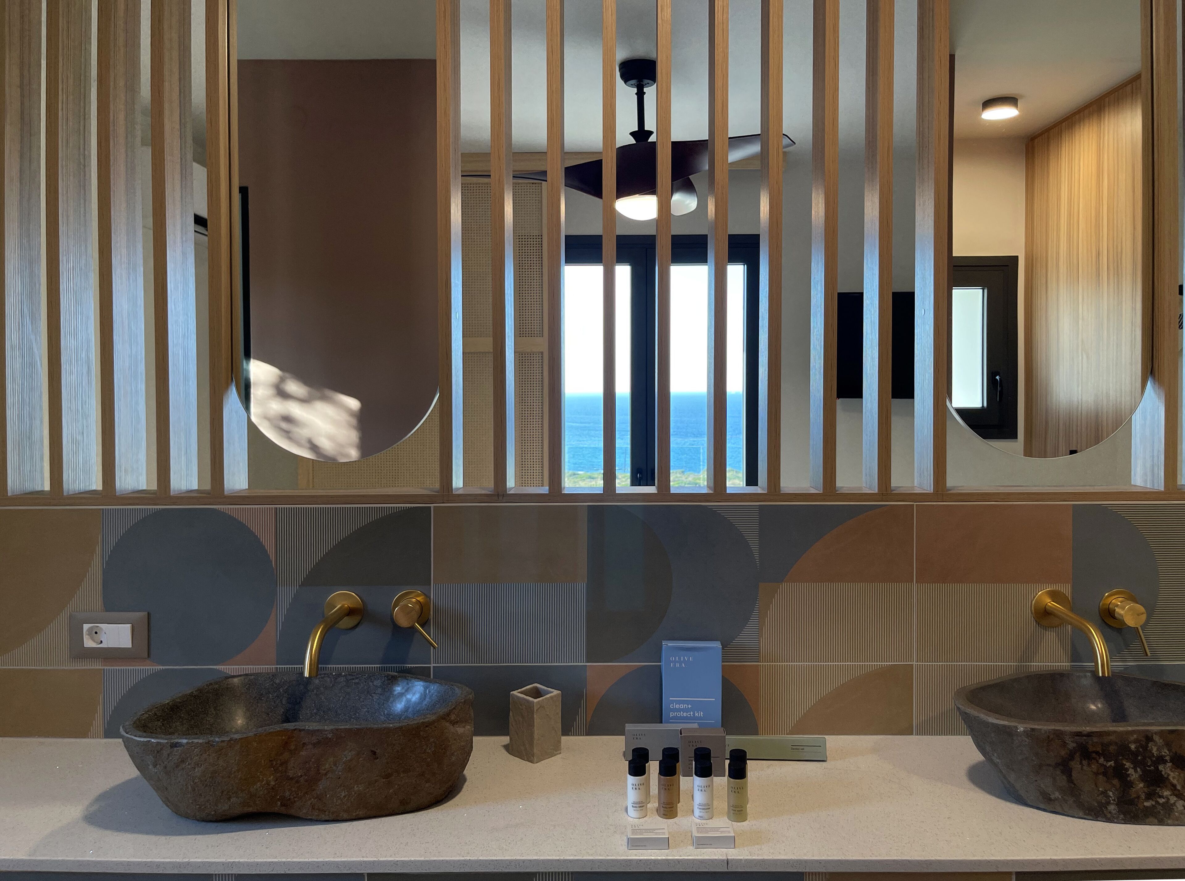 A bathroom with two stone sinks, a ceiling fan, and a view of the ocean through large windows.