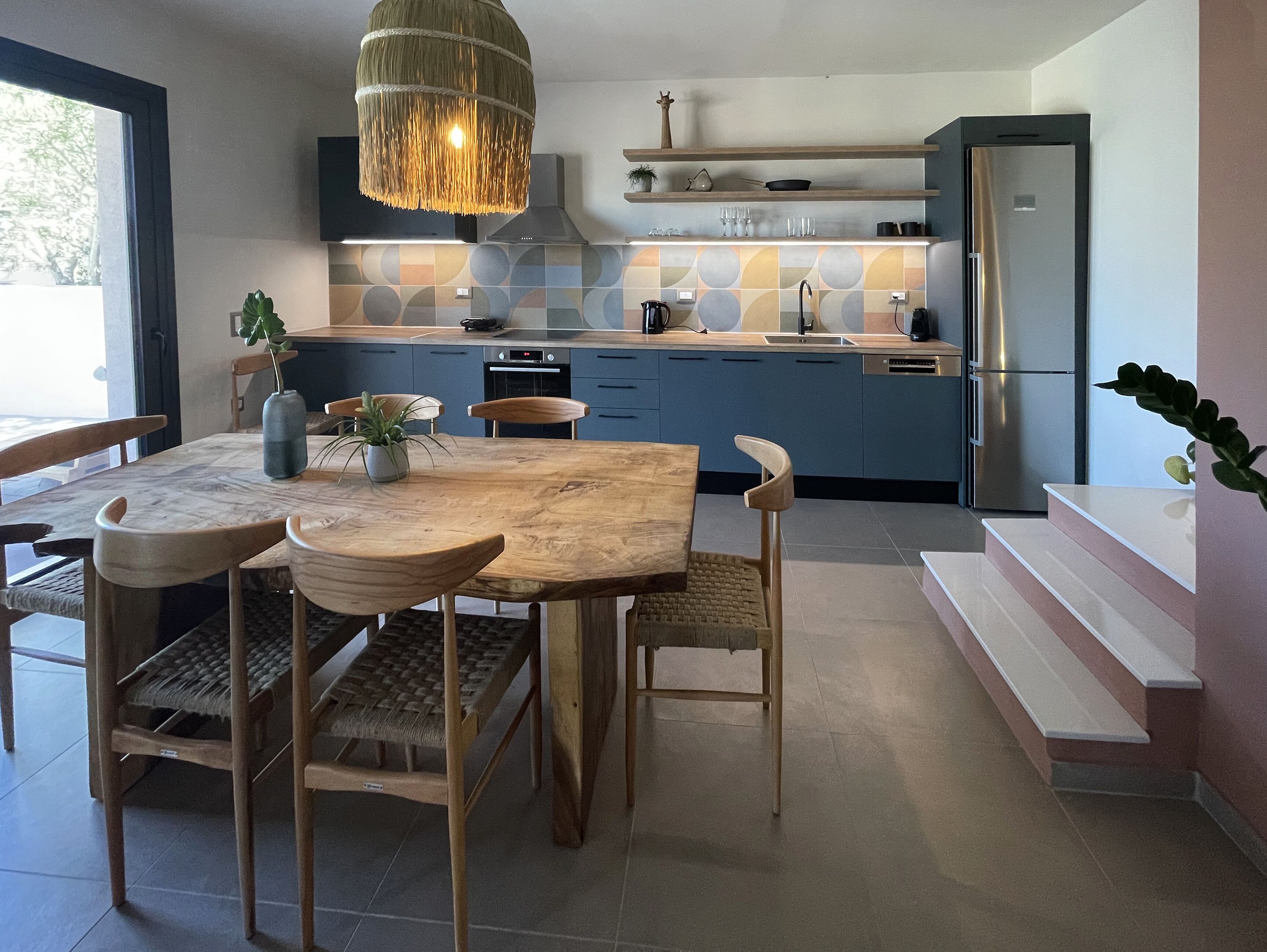 A modern kitchen with a wooden dining table, chairs, and a hanging light fixture.