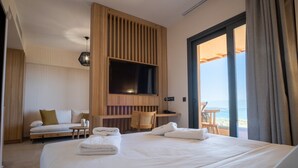 A hotel room with a large bed, a TV mounted on a wooden panel, a seating area with a sofa and chairs, and a balcony with a table.