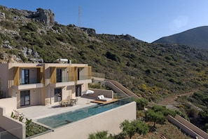 A modern house with a rooftop infinity pool, a terrace with seating, and a view of a mountainous landscape. - The Nest Resort (Hersonissos)