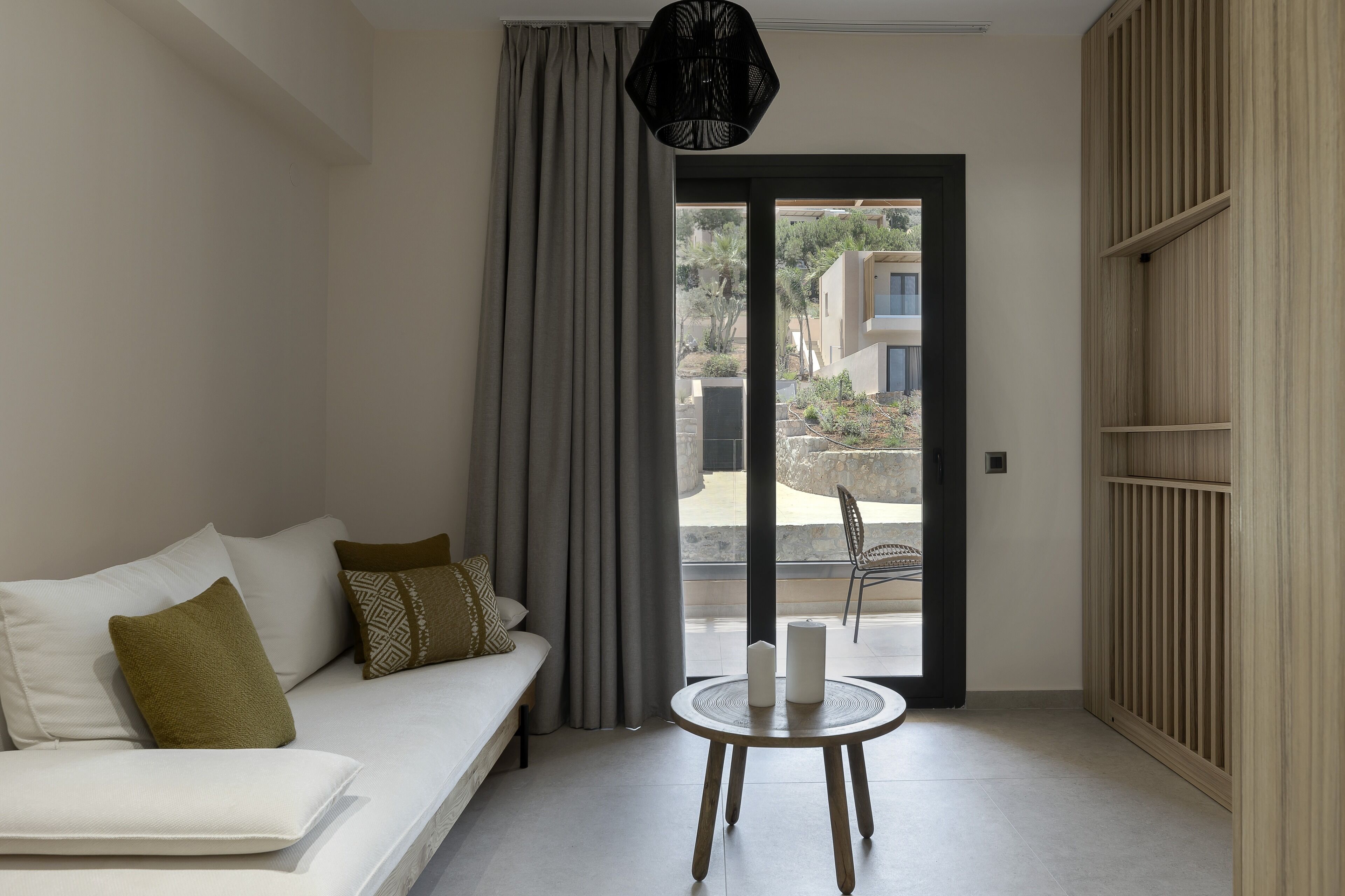 A modern living room with a sofa, a round table with candles, and a view through a glass door.