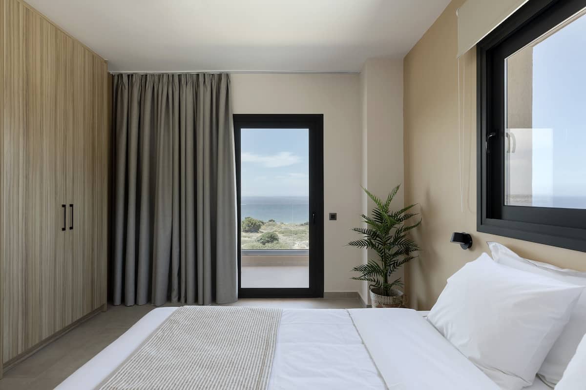 A bedroom with a bed, a wardrobe, a potted plant, and a view of the sea through a door.
