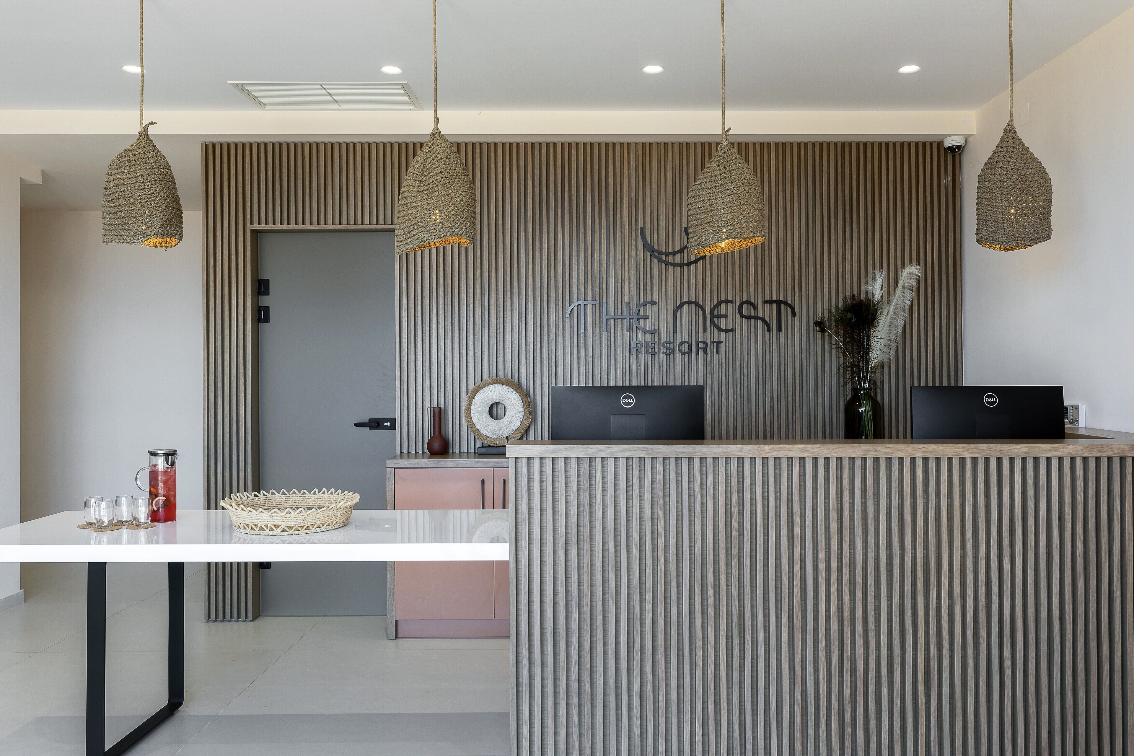 A reception area with a modern design, featuring a reception desk, two hanging pendant lights, and a wall-mounted sign that reads "The Nest Resort".