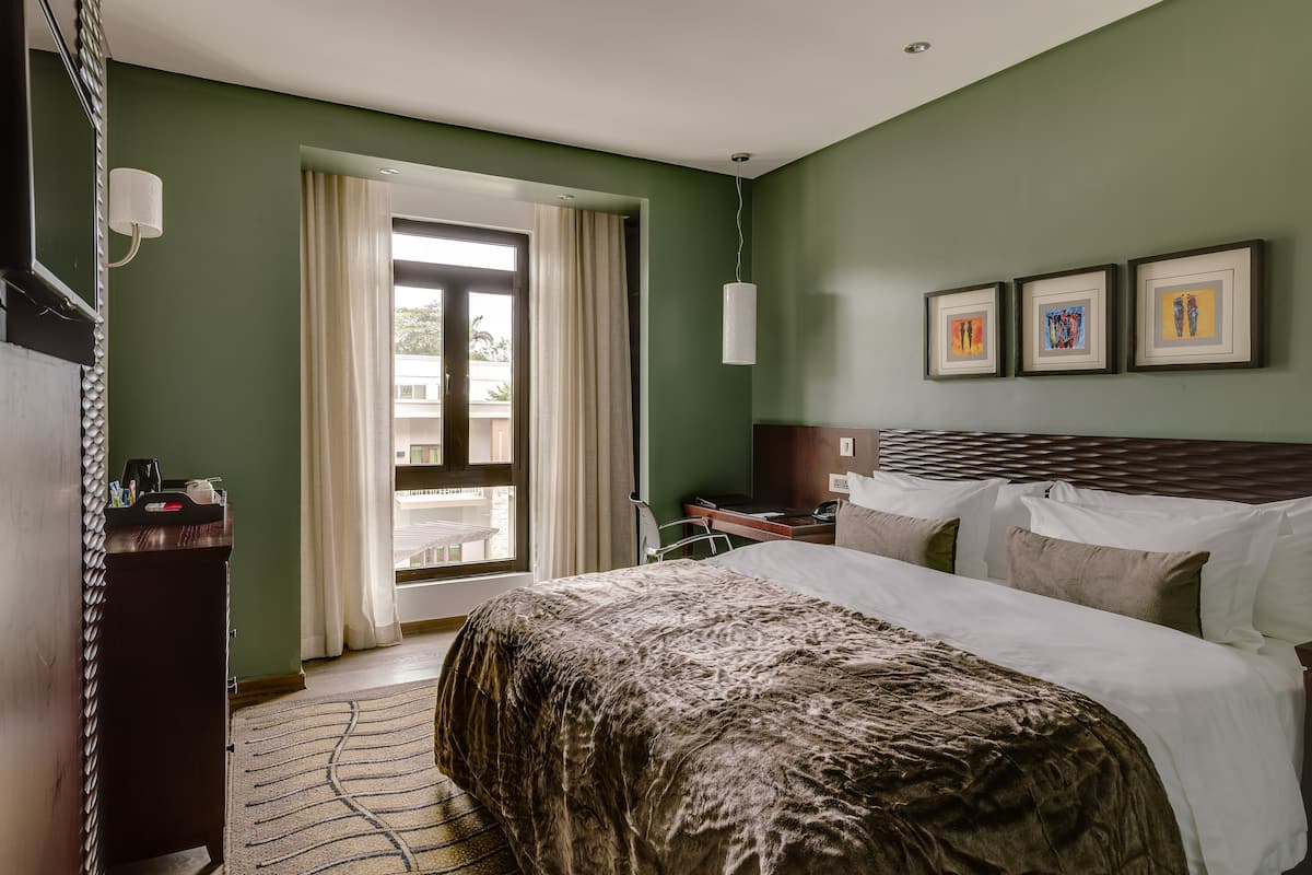 Una habitación de hotel con cama, escritorio, silla, lámpara de escritorio y ventana con cortinas.