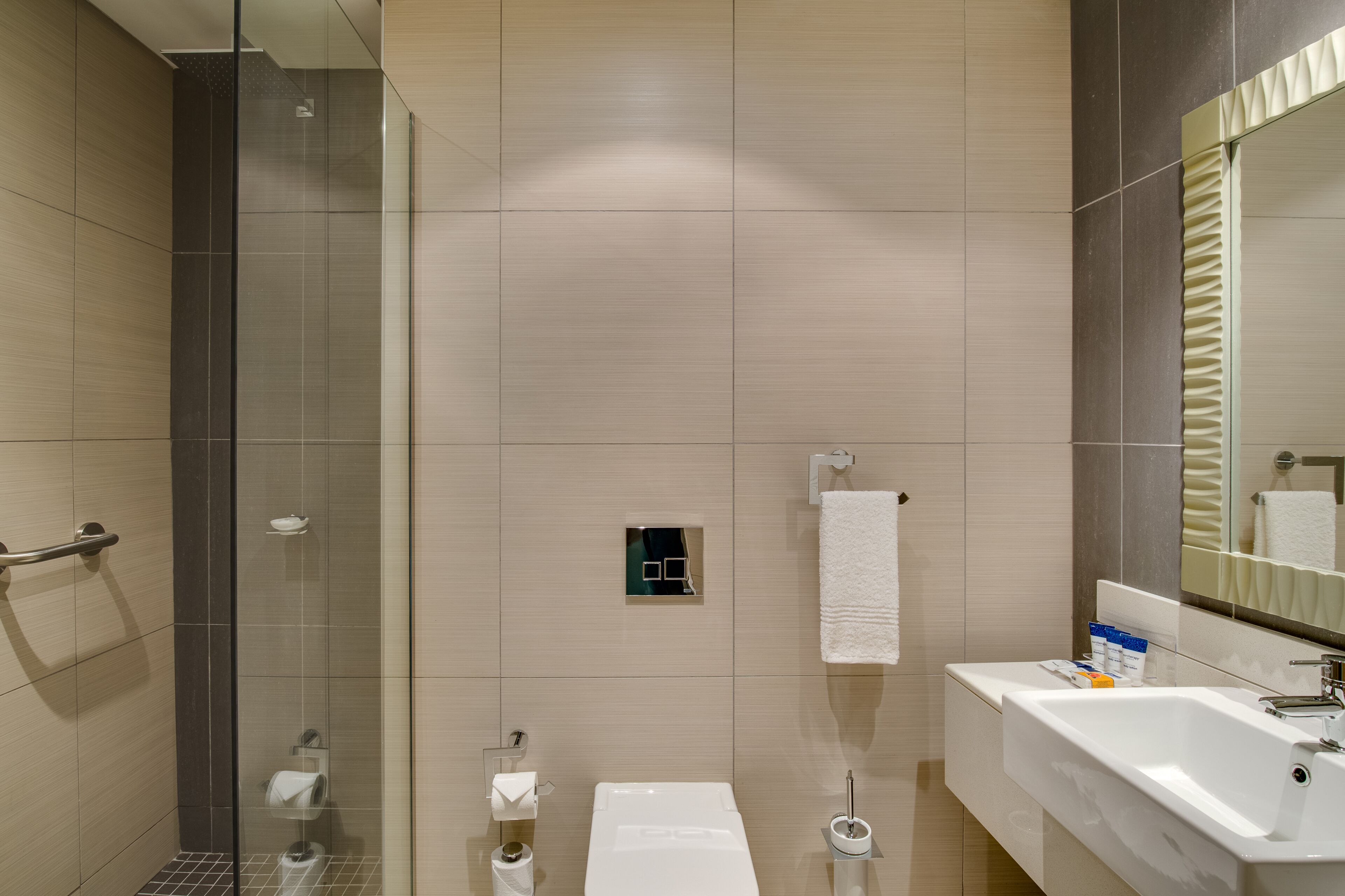 Une salle de bain moderne avec une douche à l’italienne en verre, un lavabo blanc et un grand miroir.