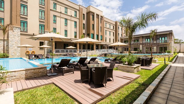 A hotel with a swimming pool, outdoor seating, and a stone facade. - Alliance by Eagles (Sekondi-Takoradi)