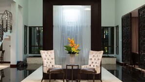 A lobby with a reception desk, two upholstered chairs, a small table with a vase of flowers, and a staircase to the left. - Alliance by Eagles (Sekondi-Takoradi)