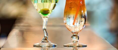 Dos cócteles sobre una superficie reflectante, con un fondo desenfocado.