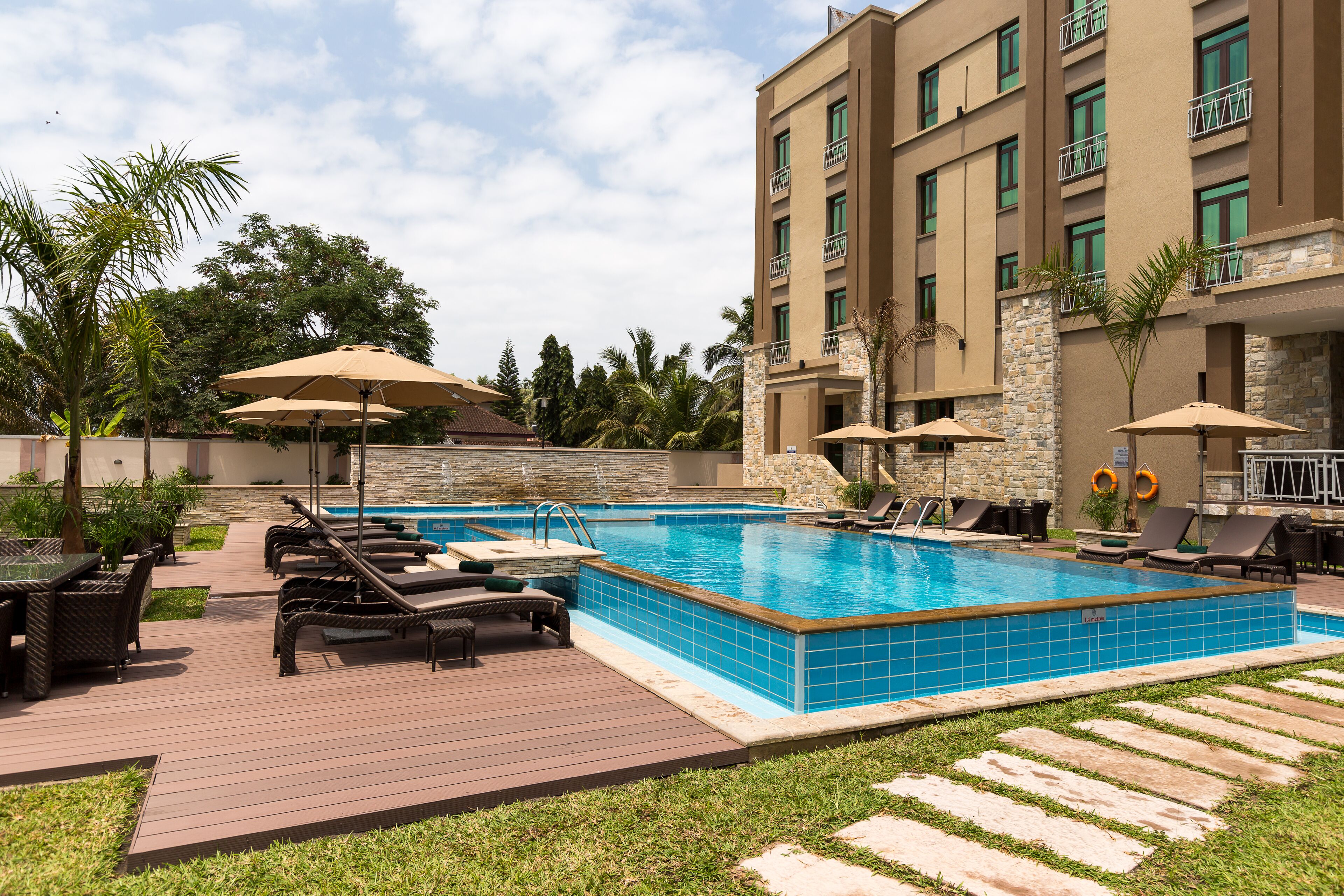A swimming pool with lounge chairs and umbrellas, surrounded by a deck and greenery.