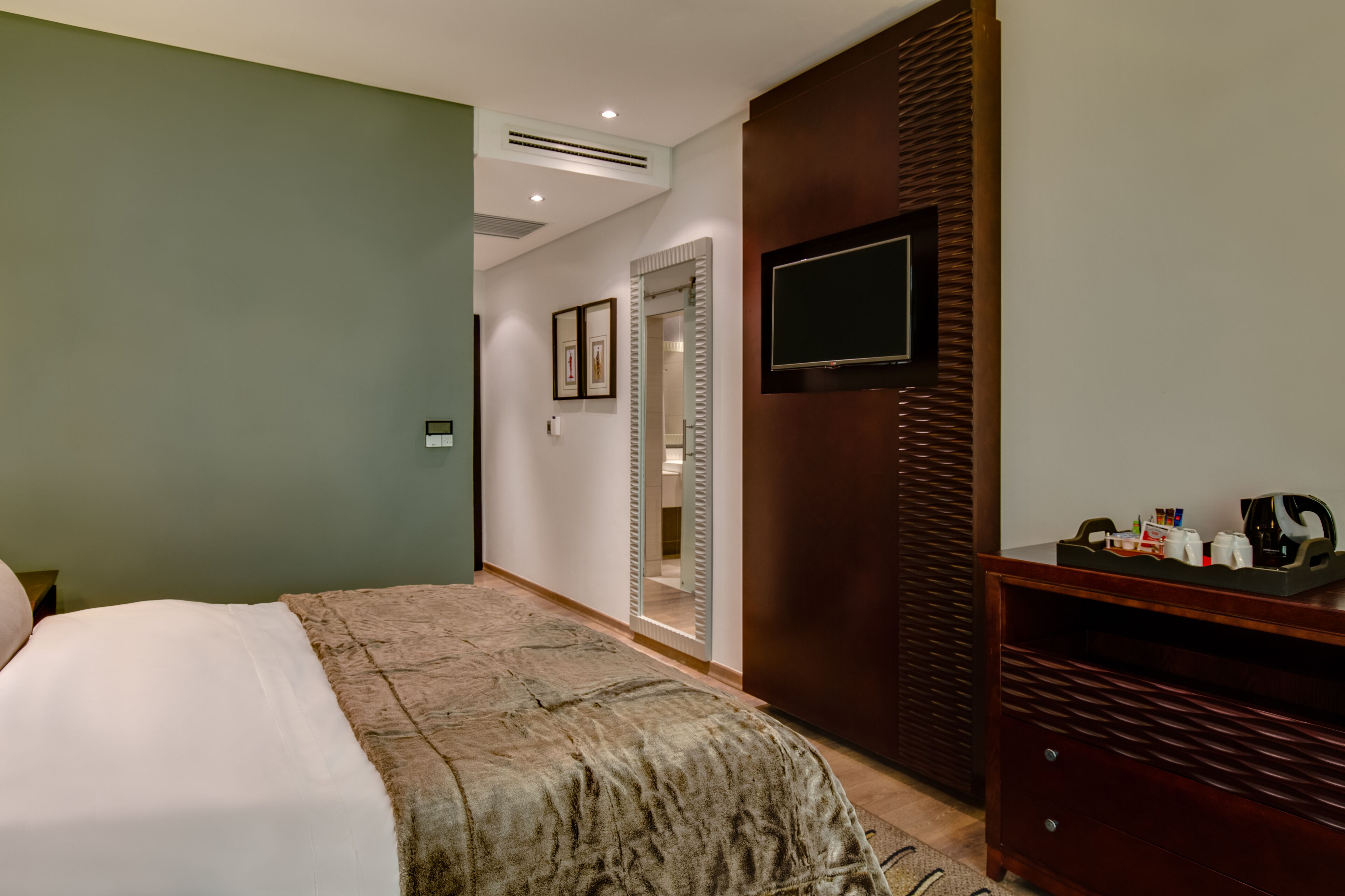 Een hotelkamer met een bed, een aan de muur bevestigde televisie, een houten dressoir en een spiegel.