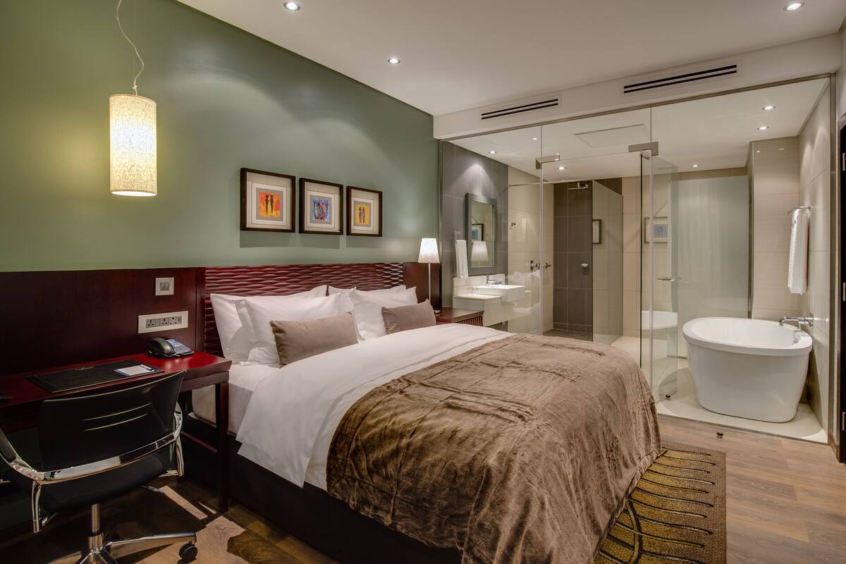 Una habitación de hotel moderna con una cama grande, un escritorio con teléfono, una silla, un baño con bañera y cabina de ducha de vidrio.