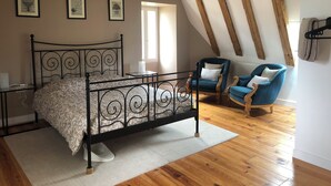 Un dormitorio con estructura de cama metálica, suelo de madera, alfombra blanca, sillón azul y una silla con cojín.