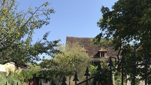 Un sendero de grava que conduce a un edificio tradicional con tejado de baldosas, rodeado de vegetación y una valla de metal.