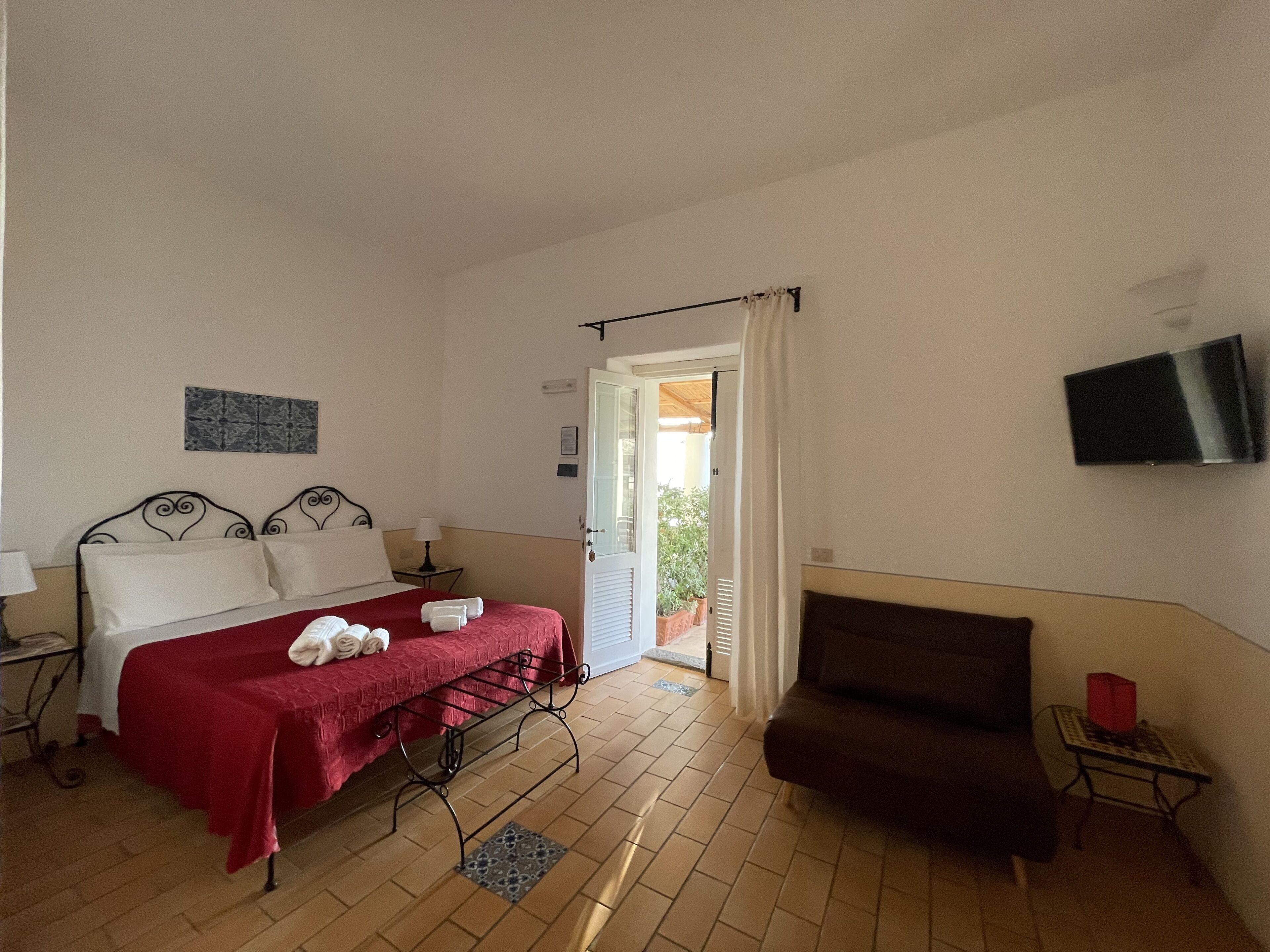 Un dormitorio con cama, una silla, un televisor y una puerta que da a un balcón.