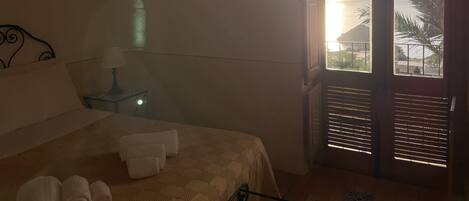 A hotel room with a bed, a nightstand, a lamp, a framed picture on the wall, and a view of the sea through the window.