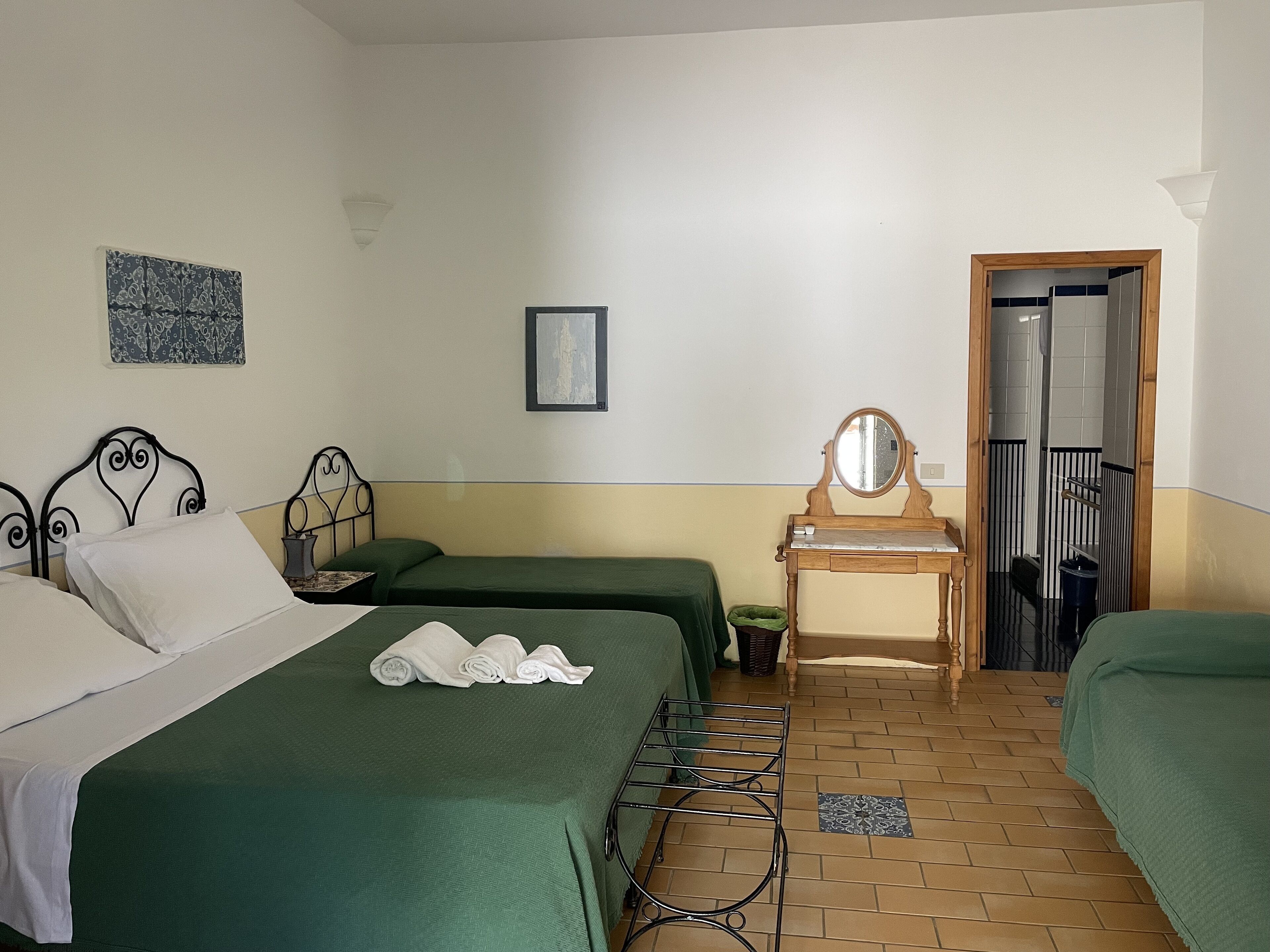 Une chambre avec deux lits simples, une commode en bois avec un miroir, une petite table et un luminaire fixé au mur.