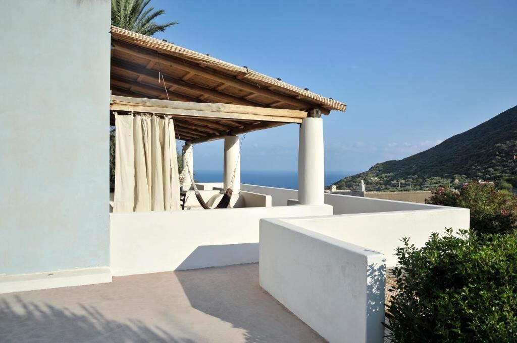Eine Dachterrasse mit einer Holzpergola, weißen Wänden und Blick auf das Meer und die Hügel.