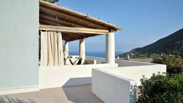 Eine Dachterrasse mit einer Holzpergola, weißen Wänden und Blick auf das Meer und die Hügel.