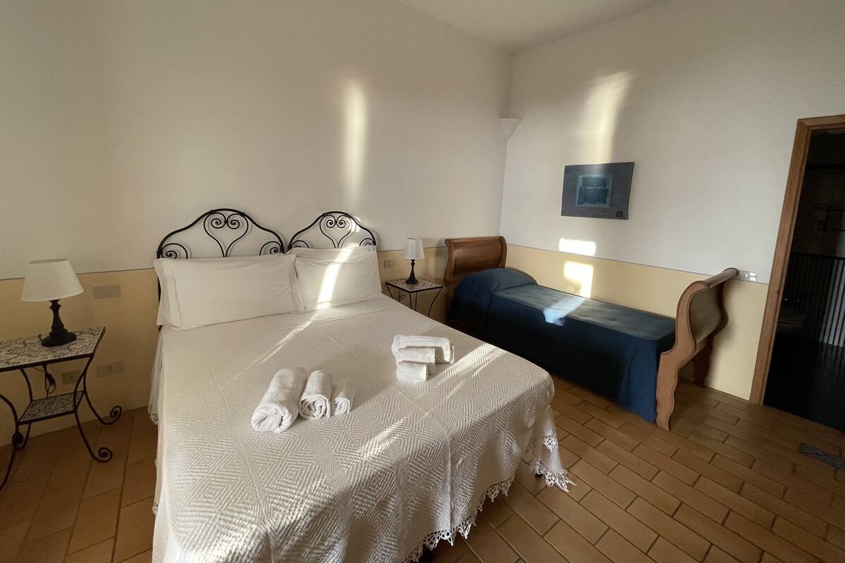 A hotel room with a bed, a small table, a chair, and a wall-mounted picture.