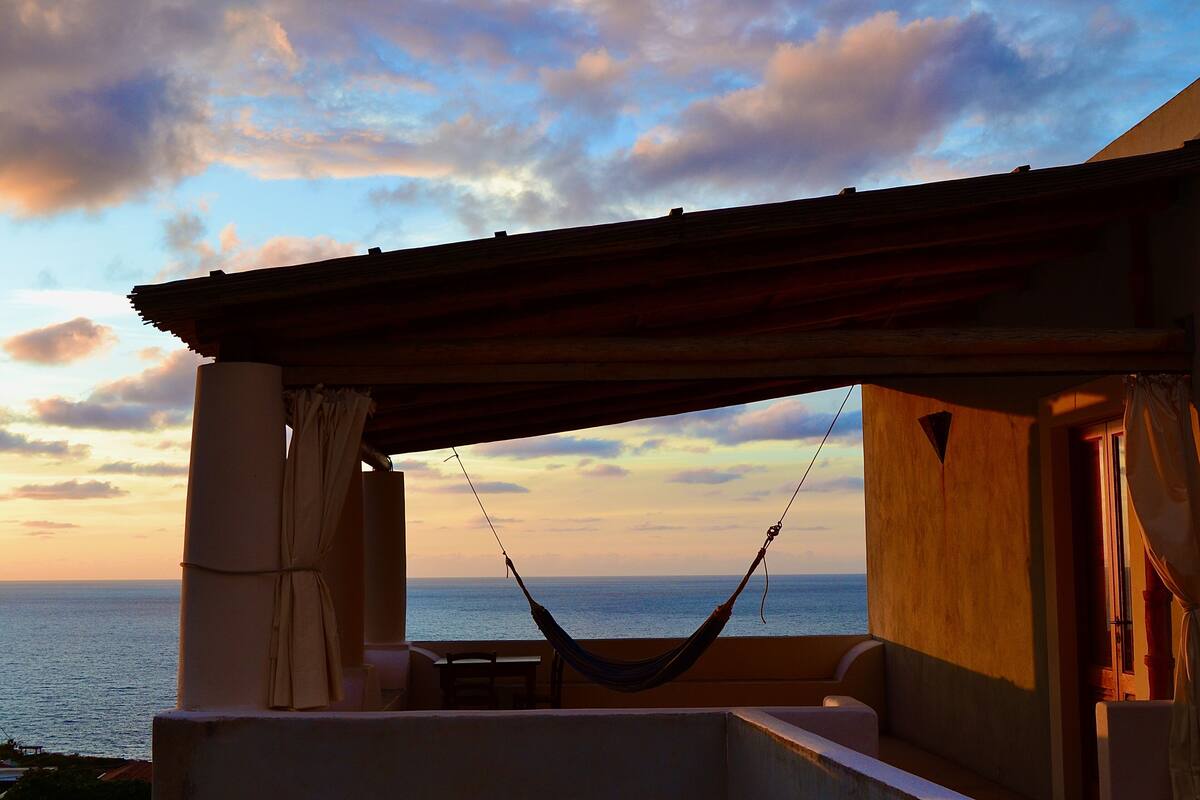 A hammock on a balcony with a view of the sea and a sunset.